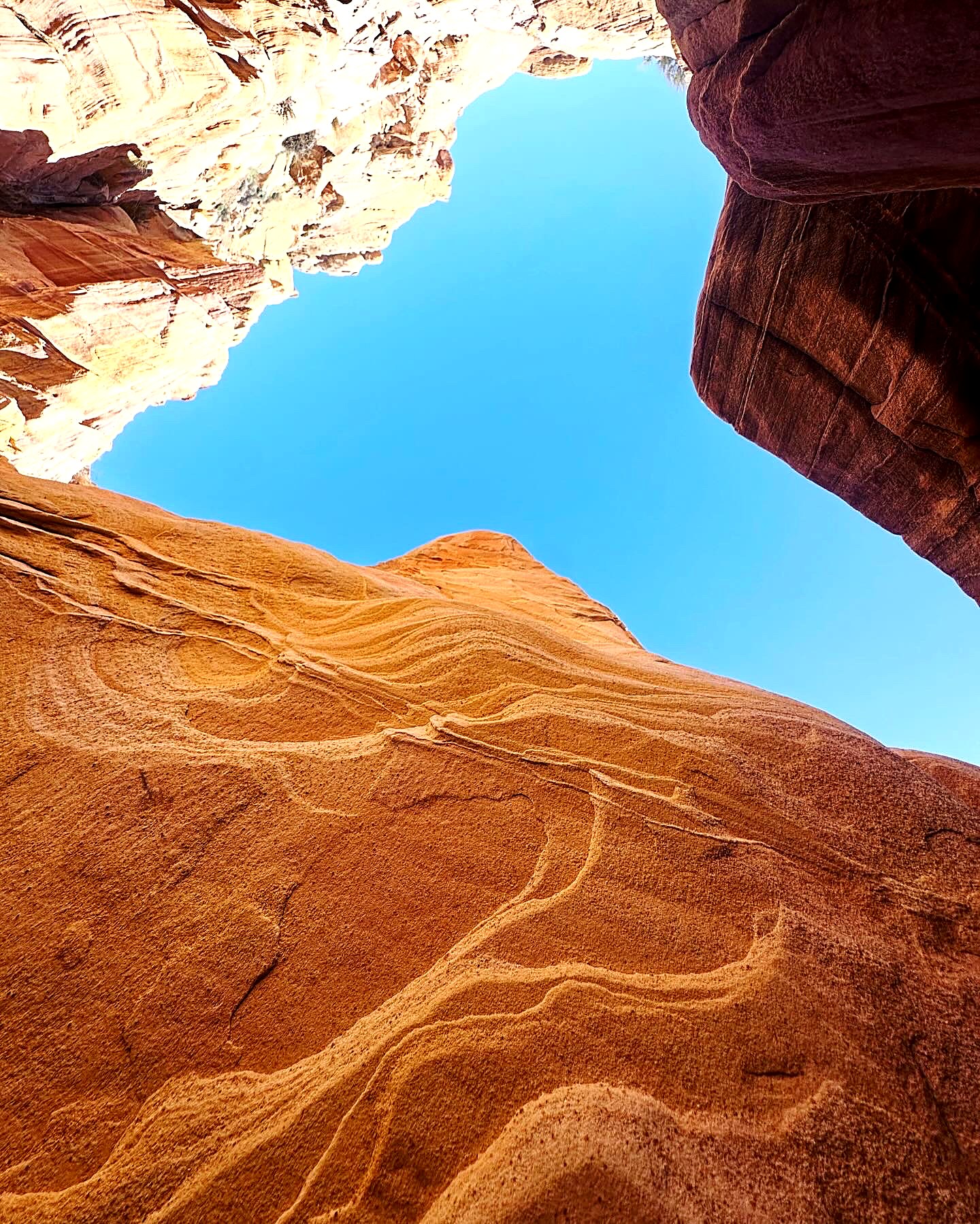 Looking up at curving wave patterns in orange sandstone against blue sky
