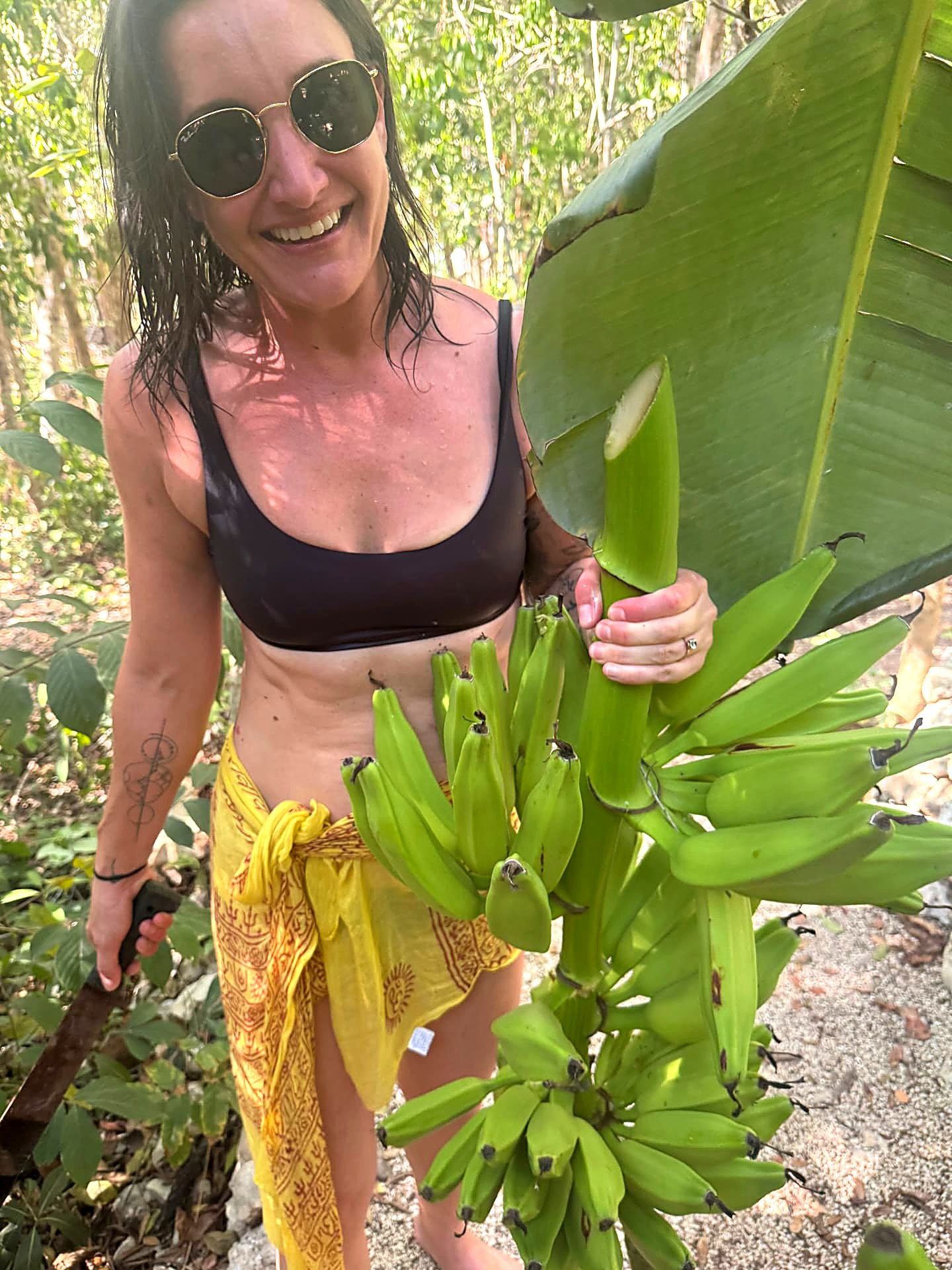 Esther holding a freshly cut stalk of green bananas in the jungle