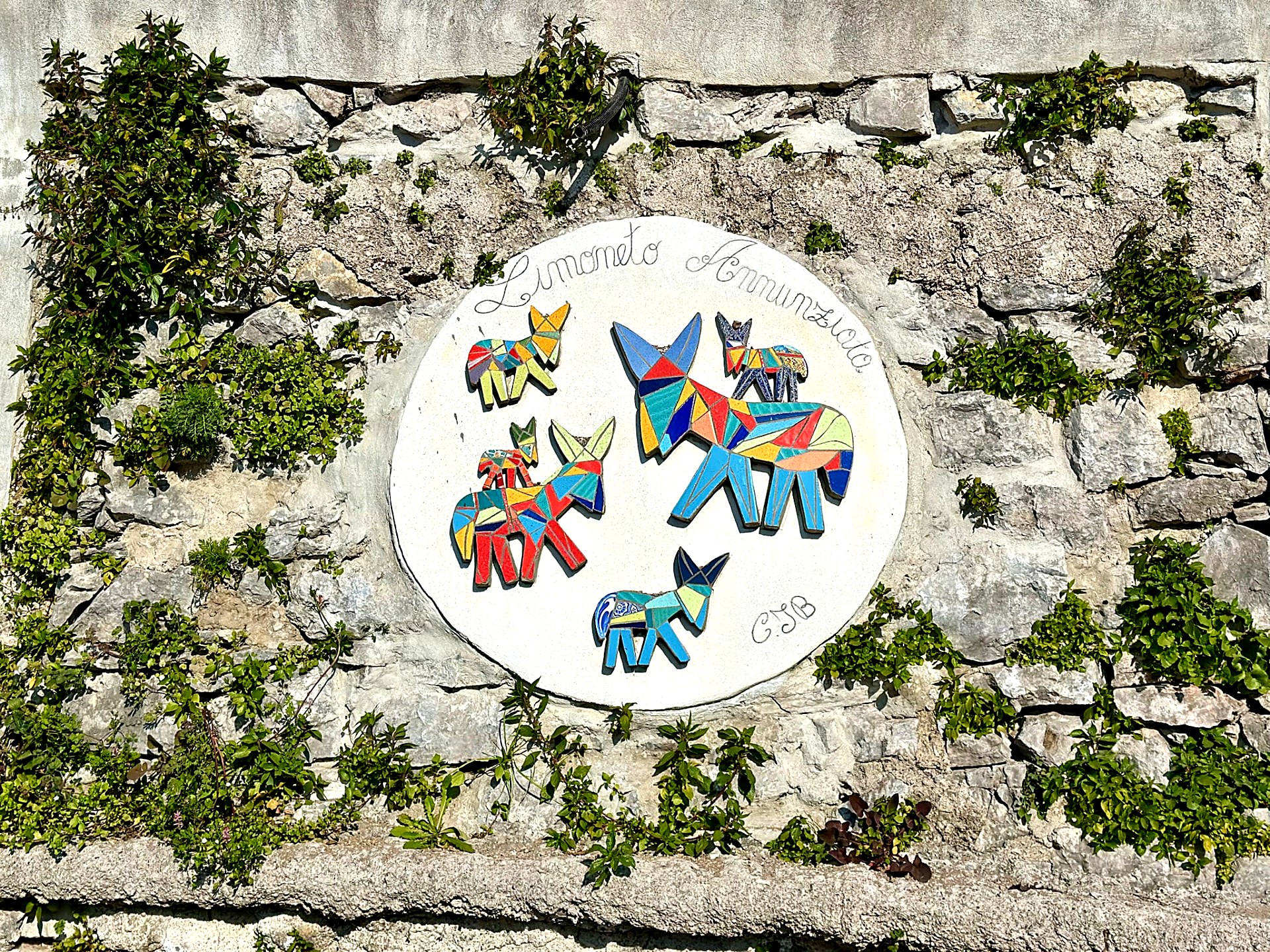 Colorful ceramic tile artwork mounted on a mossy stone wall