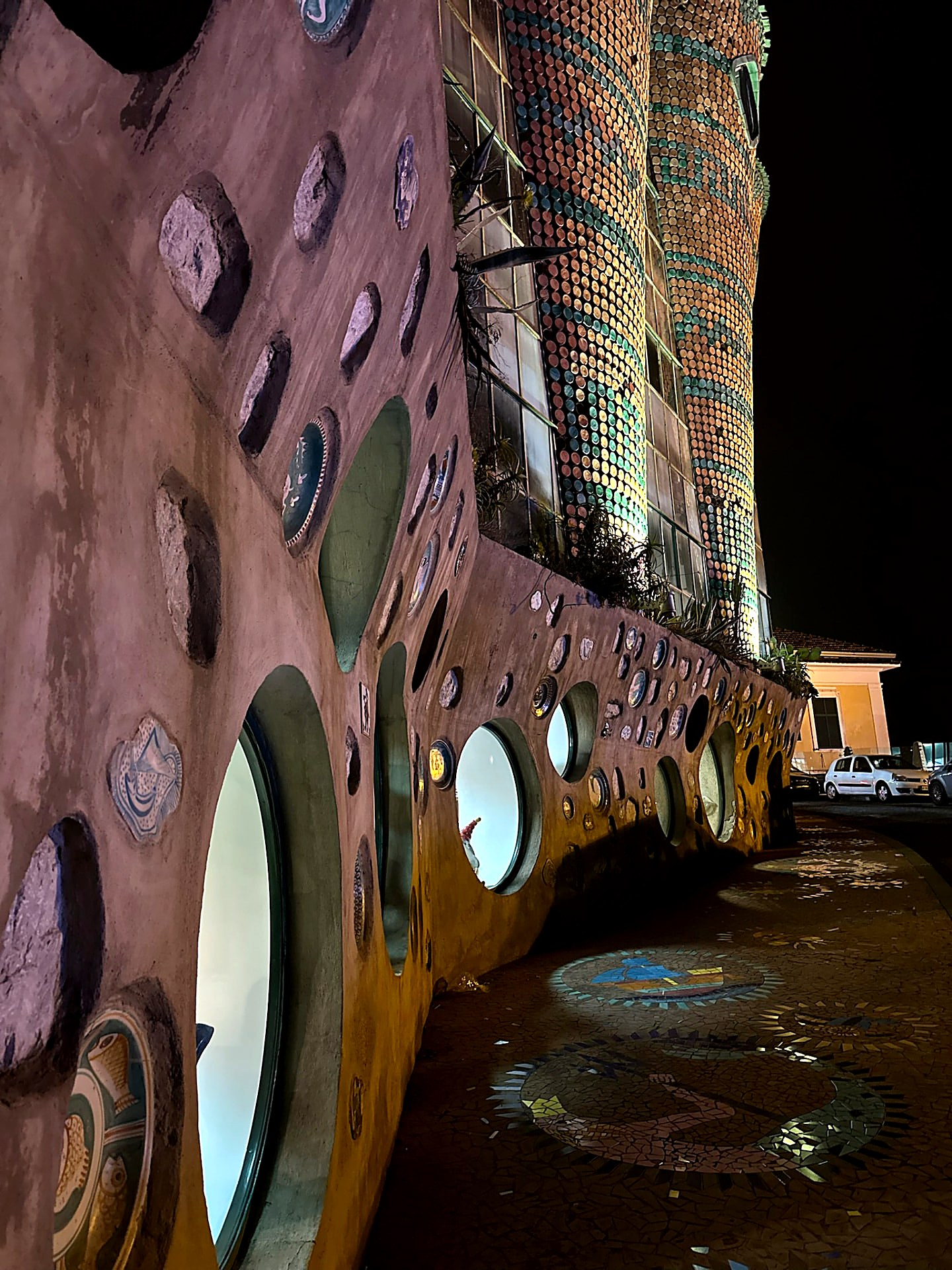 Curved building facade embedded with ceramic plates and stones at night