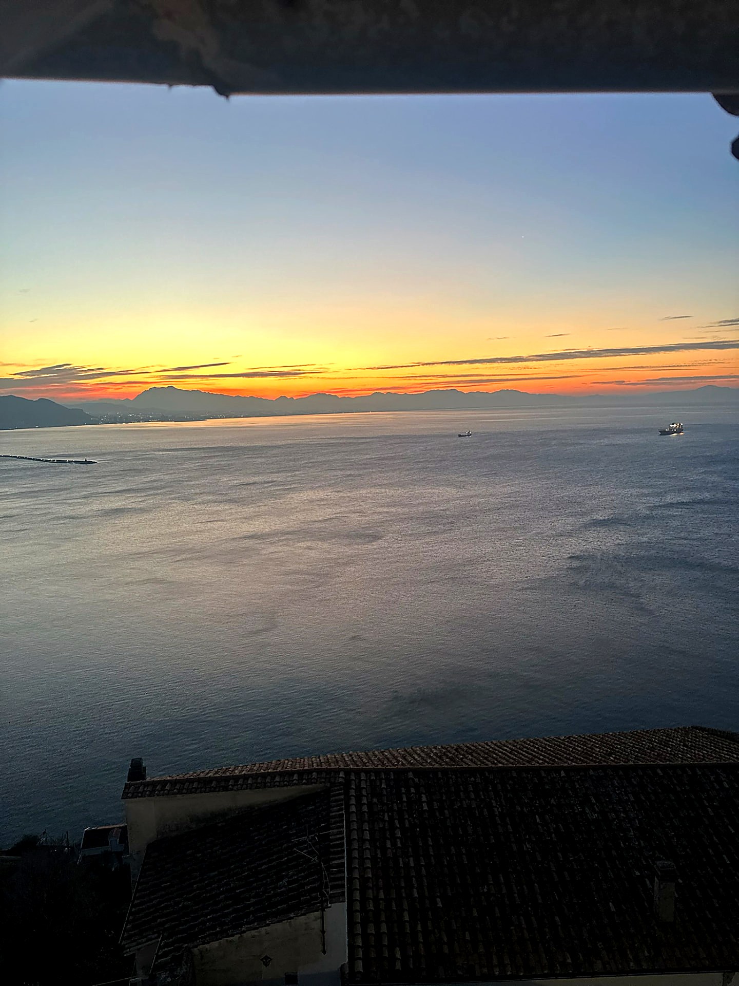 Sunrise over a calm sea with mountains on the horizon