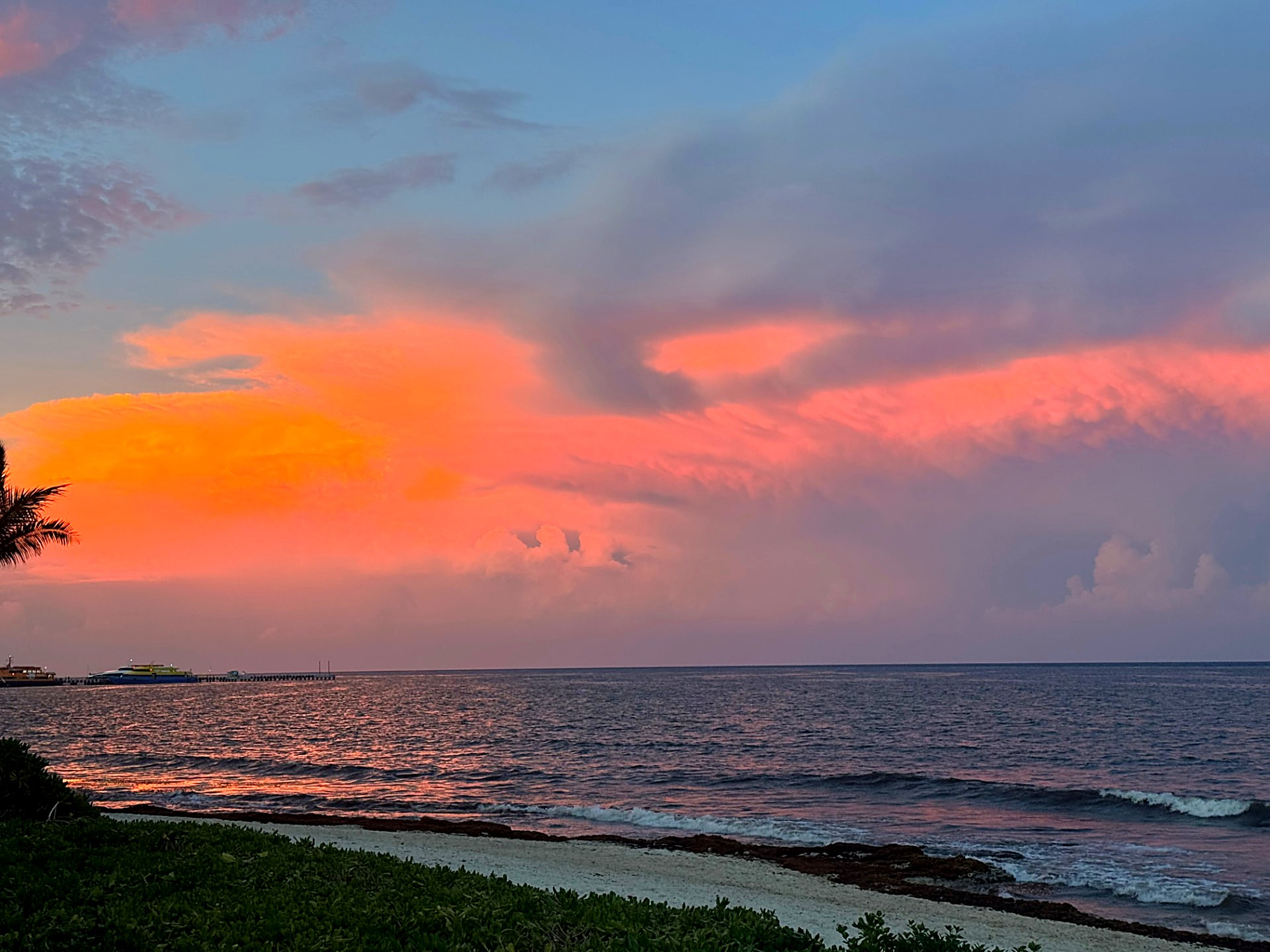 Orange sunset clouds over the sea with a pier in the distance